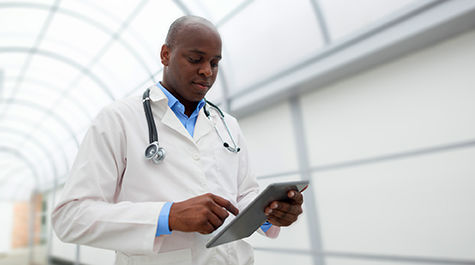 Male doctor reviewing tablet content while walking down medical center hallway